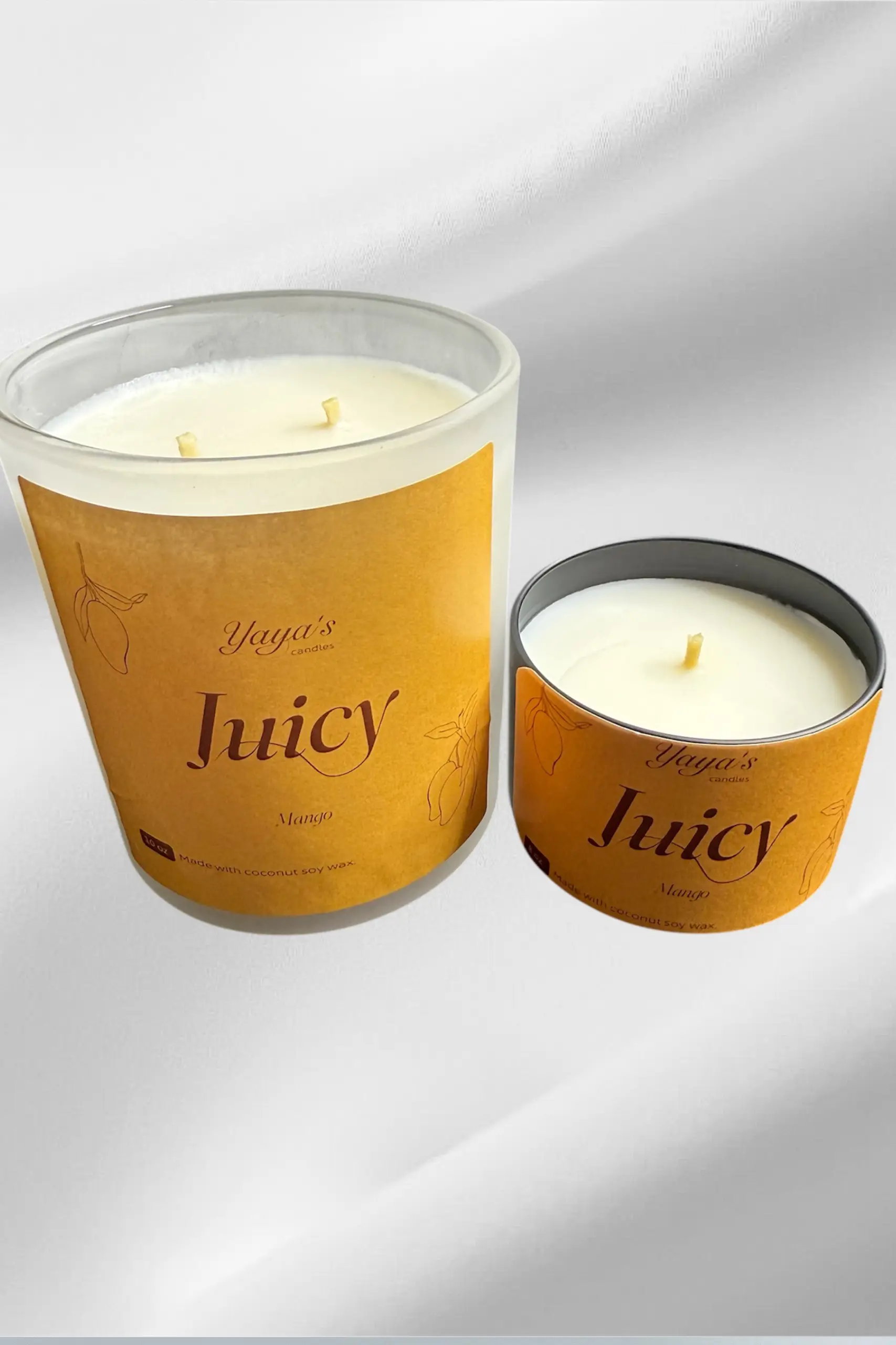 Two mango-scented candles from Yaya's Candles, featuring a large glass jar with two wicks and a small metal tin.Two mango-scented candles from Yaya's Candles, featuring a large glass jar with two wicks and a small metal tin.