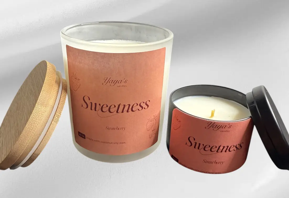 Two candles labeled "Sweetness - Strawberry," one in a glass jar with a wooden lid and the other in a black tin.