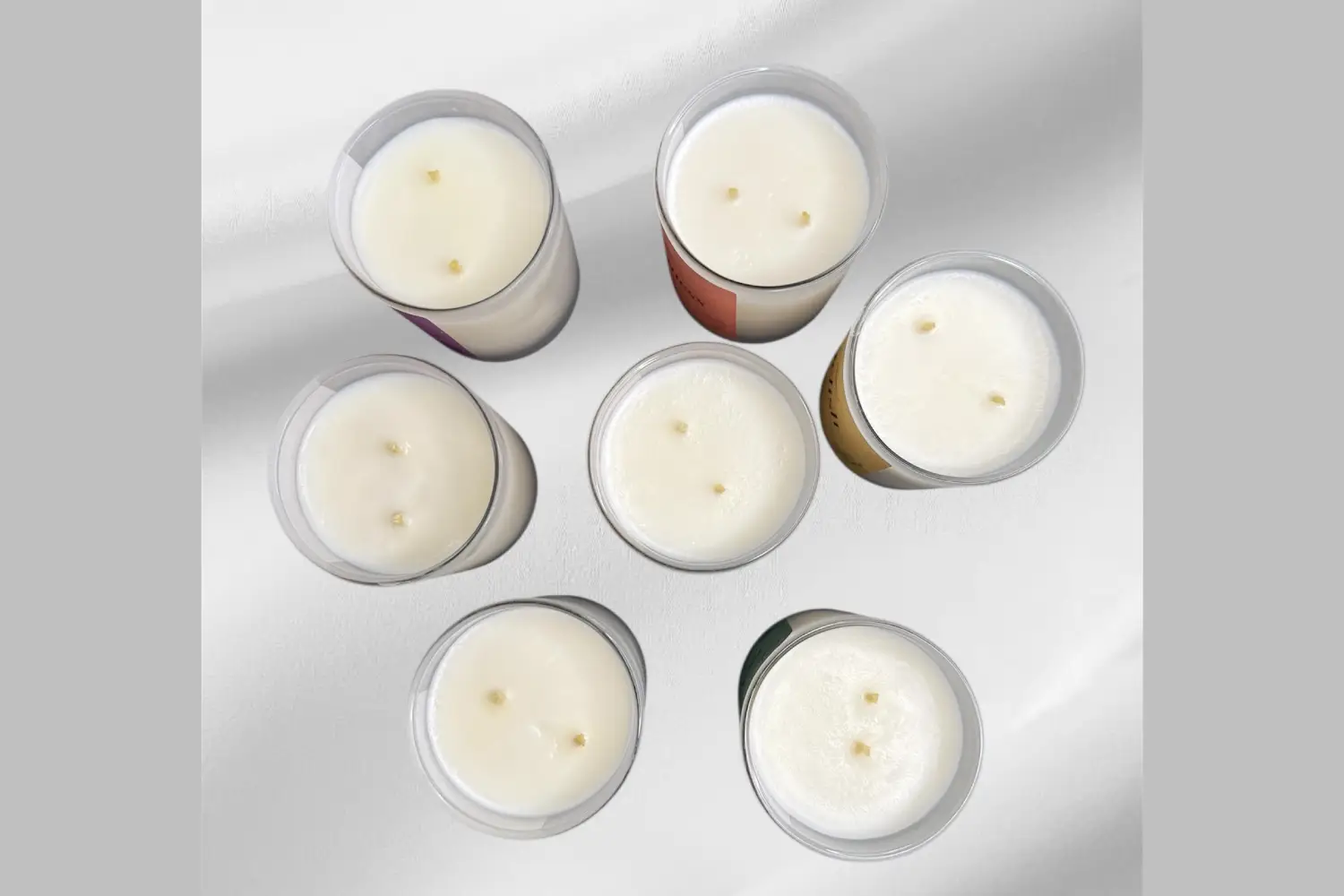 banner-image-yaya-1pt A collection of six scented candles with white wax and varying colored labels, arranged in a circular pattern.