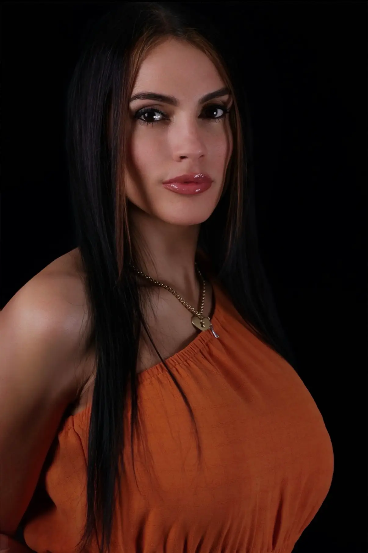 IMG_0938 webp A woman with long, straight black hair wearing an orange off-shoulder top stands against a dark background, exuding confidence.